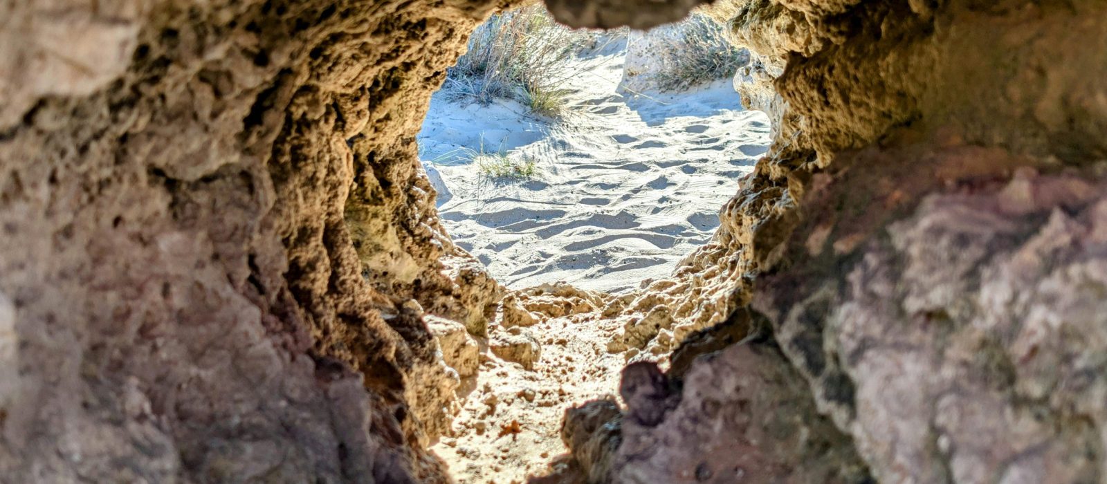 View of a sandy beach through a natural rock formation, capturing erosion effects.